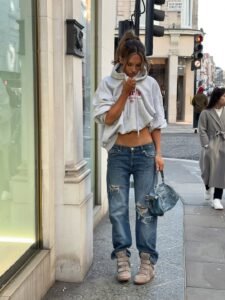woman in grey cropped hoodie and ripped blue jeans holding a light blue handbag