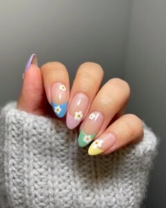 multi-colored pastel french tip nails with small white daisy floral accents on a hand