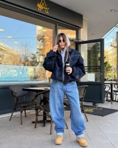 woman wearing blue barrel jeans, oversized black jacket, grey hoodie, and tan work boots.