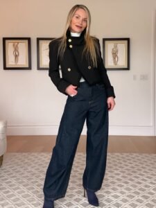 woman wearing black cropped jacket and dark wash barrel jeans in a modern living room.