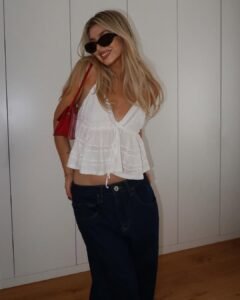 blonde woman in white lace camisole and baggy jeans with red bag