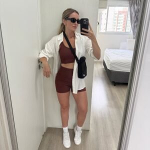 woman in brown athletic set and white shirt taking mirror selfie
