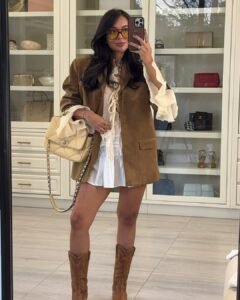 woman in a brown suede blazer and ruffled white dress with cowboy boots