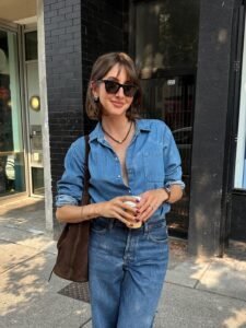 woman in a blue denim button-down shirt and matching jeans holding a coffee cup outdoors