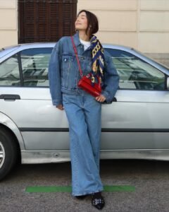 woman leaning against silver car wearing oversized denim jacket and wide leg jeans