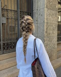 woman in a white shirt seen from behind with a long blonde and brown french braid.