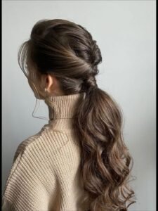 woman wearing a beige turtleneck sweater with her brown hair in a twisted low ponytail.