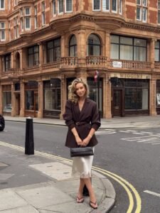 woman in a brown belted blazer and cream silk lace skirt on a city street
