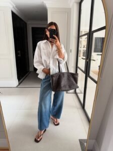 woman in white button down shirt and blue barrel leg jeans with woven tote bag.
