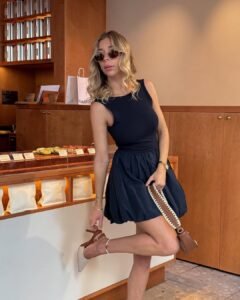 woman in a navy bubble hem dress and pointed heels adjusting her shoe in a cafe