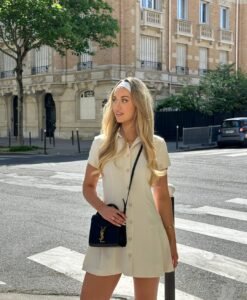 woman in a short cream button-down dress and white headband standing on a city crosswalk