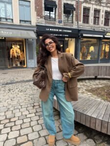 woman in light blue barrel jeans, tan checkered blazer, and platform boots on cobblestone.