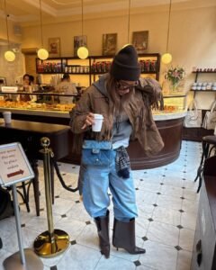 woman in brown fringe jacket and light wash jeans holding coffee cup