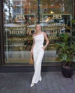 woman in white one shoulder top and trousers in front of bakery