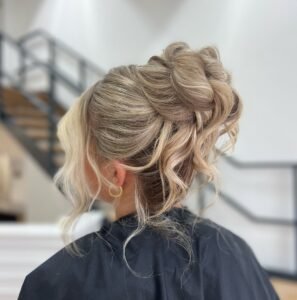 back view of an elegant blonde messy bun updo with loose curled strands framing the face.