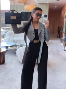 woman in a grey pinstripe cropped blazer holding a black handbag in a luxury showroom