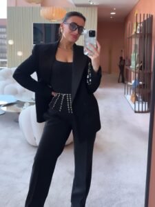 woman in a black tailored suit and glasses taking a mirror selfie in a showroom