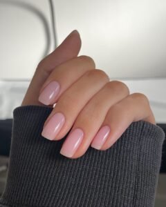 short square light pink glossy gel nails on a hand with a dark sleeve