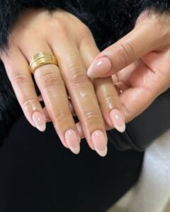 natural nude french tip manicure on almond shaped nails with gold rings.