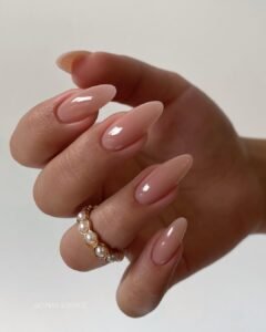 long glossy nude almond nails accessorized with a gold ring featuring small white pearls.