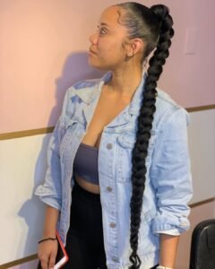 woman wearing a light blue denim jacket with a very long thick black braided ponytail.