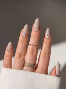 glossy beige almond nails decorated with small white daisy floral accents and gold centers.