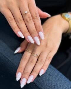milky white almond shaped nails on hands with gold rings and a watch.