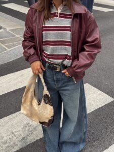 person wearing wide leg barrel jeans, burgundy leather jacket, striped shirt, and patterned bag.