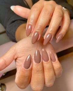 glossy almond shaped brown builder gel nails on a person with warm skin tones.