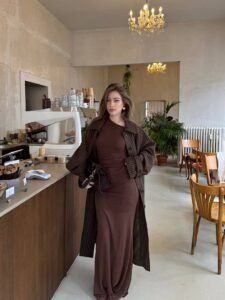 woman in brown maxi dress and pinstripe coat inside modern cafe
