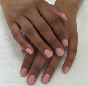 glossy sheer pink polish on short natural nails over a clean white towel background.