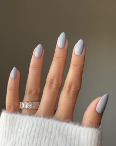 light grey almond shaped manicure on a hand wearing a gold stackable ring.