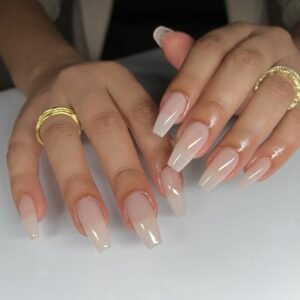 long sheer nude coffin shaped gel nails on hands wearing gold rings.