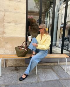 woman in a yellow striped shirt and blue jeans sitting on a bench with coffee