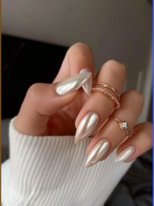 iridescent white chrome stiletto nails on a hand wearing gold rings and white sweater