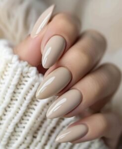 glossy tan almond shaped nails held against a white chunky knit sweater sleeve.