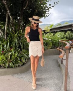 woman wearing a black tank top, tan crochet mini skirt, and a straw boater hat