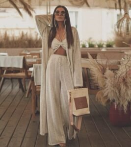 woman wearing tan crochet knit three-piece resort wear set and holding straw tote bag