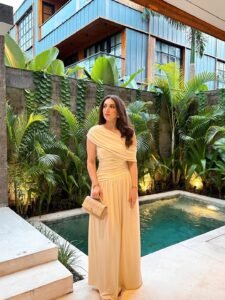 woman in cream off-the-shoulder maxi dress standing by tropical pool with lush greenery