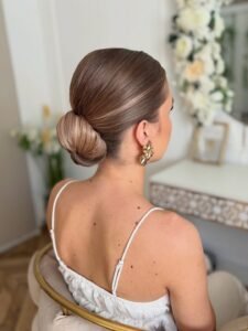 sleek low bun hairstyle with smooth light brown hair and gold earrings