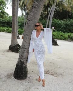 woman in long-sleeved white lace maxi dress leaning against palm tree on sandy beach