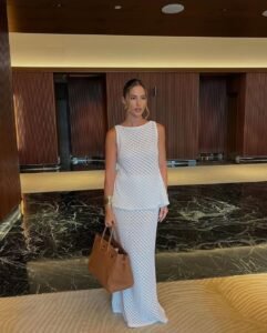 woman in white sleeveless crochet top and matching maxi skirt holding brown leather tote