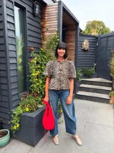 woman in leopard print puff sleeve top and blue barrel jeans with red bag.