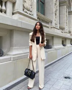 woman in a cream blazer and matching trousers posing against a classic stone building.