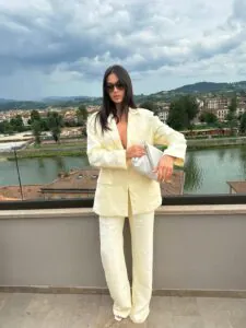 woman wearing a yellow linen suit and sunglasses standing on a balcony overlooking a river