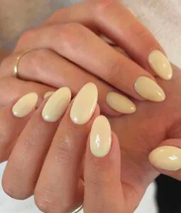 light butter yellow almond nails on a hand with a thin gold wedding band.