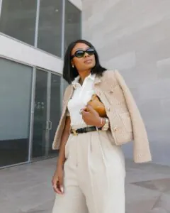 woman wearing a beige tweed jacket over a white polo shirt and high-waisted cream trousers