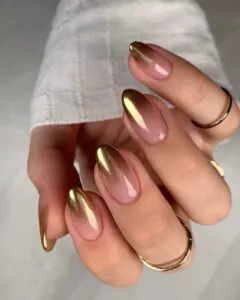 pink to gold metallic ombre almond nails with thin gold rings on one hand.