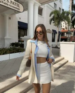 woman in a beige blazer and white mini skirt walking past white columns in the city