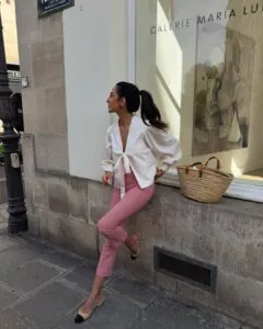 woman in a white tie-front blouse and red gingham capri pants leaning against a wall.